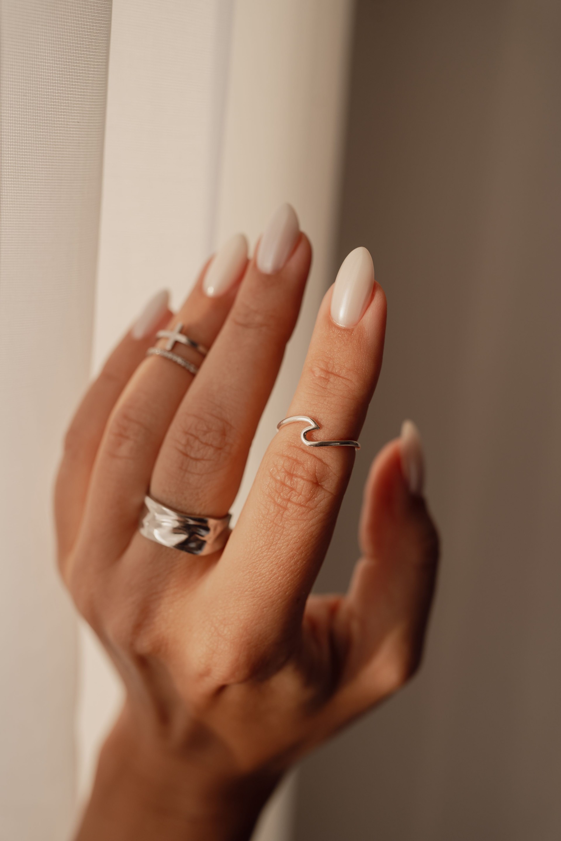 Vertical shot of a young woman's hand with elegant silver rings and nude manicure with chrome polish